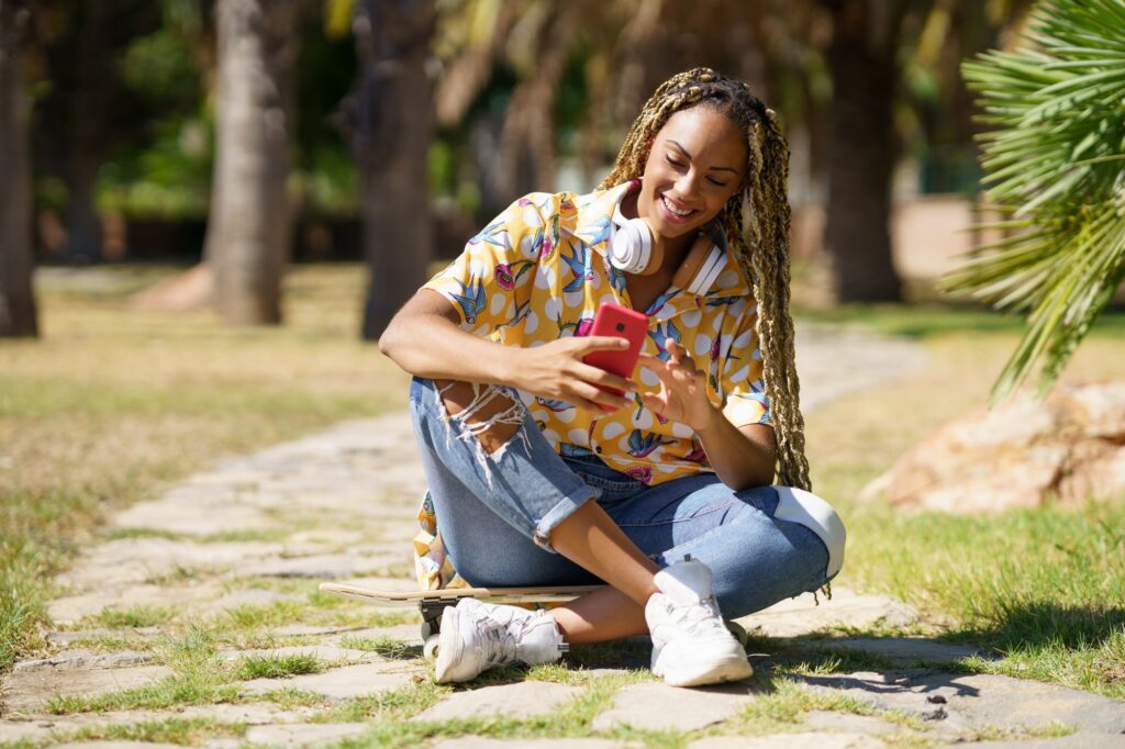 African girl using a smartphone sitting on her skateboard in the street